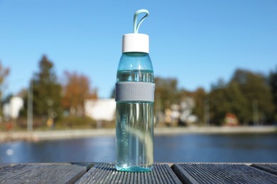 Photo of Glass bottle with water on wooden pier near river outdoors
