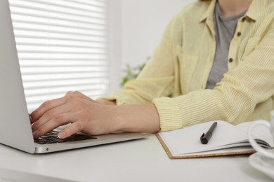 Home workplace. Woman typing on laptop at white desk indoors, closeup