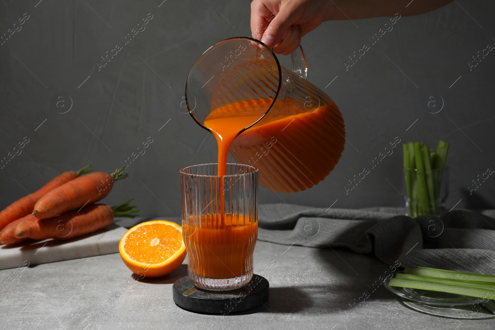 Photo of Woman pouring carrot juice from jug into glass at light grey table, closeup