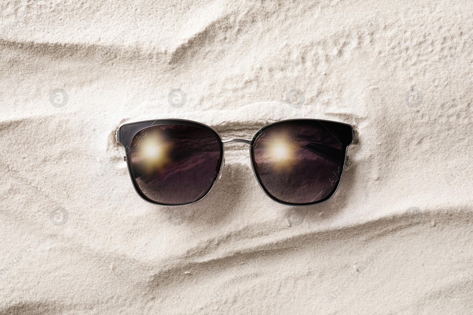 Photo of Stylish sunglasses on white sand, top view