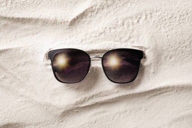 Stylish sunglasses on white sand, top view