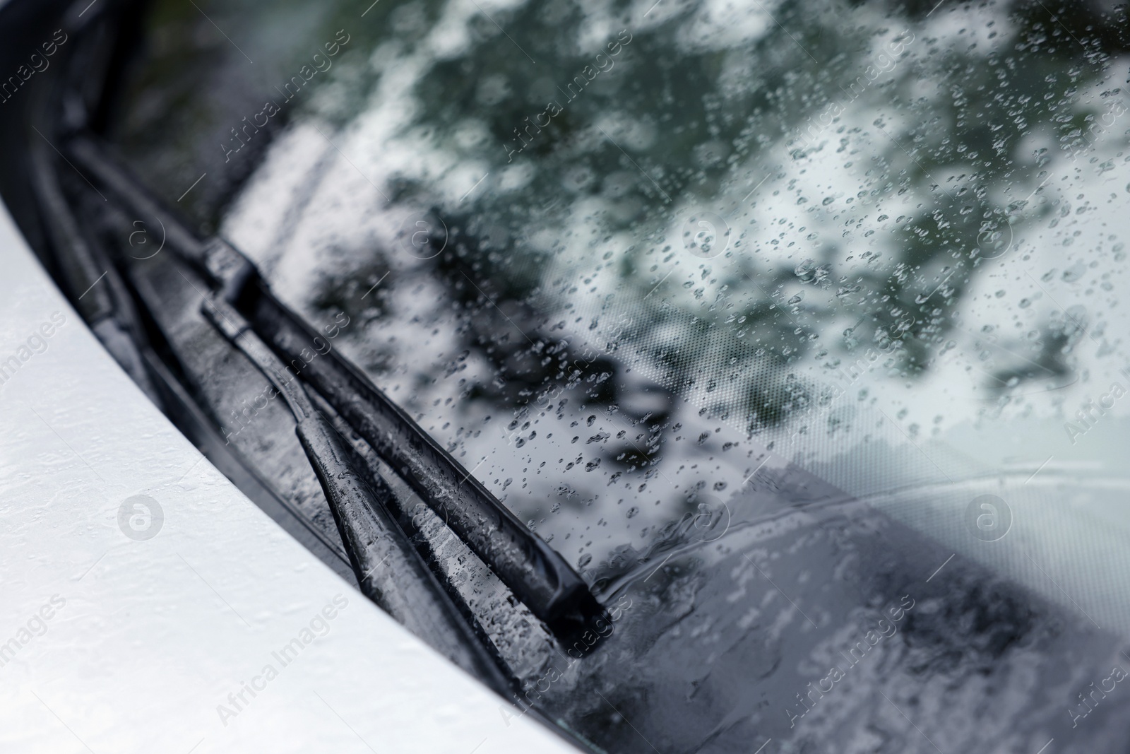 Photo of Wipers cleaning raindrops from car windshield outdoors