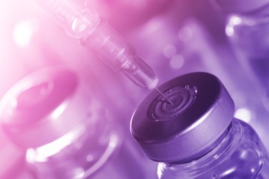 Image of Filling syringe with medicine from vial against blurred background, closeup. Color toned