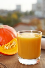 Photo of Glass with tasty pumpkin juice on wooden board indoors, closeup