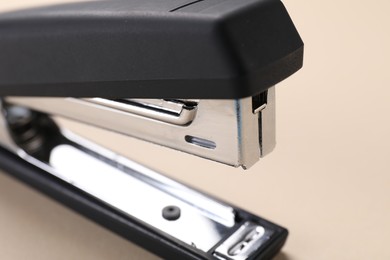 Photo of Black stapler with staples on beige background, closeup