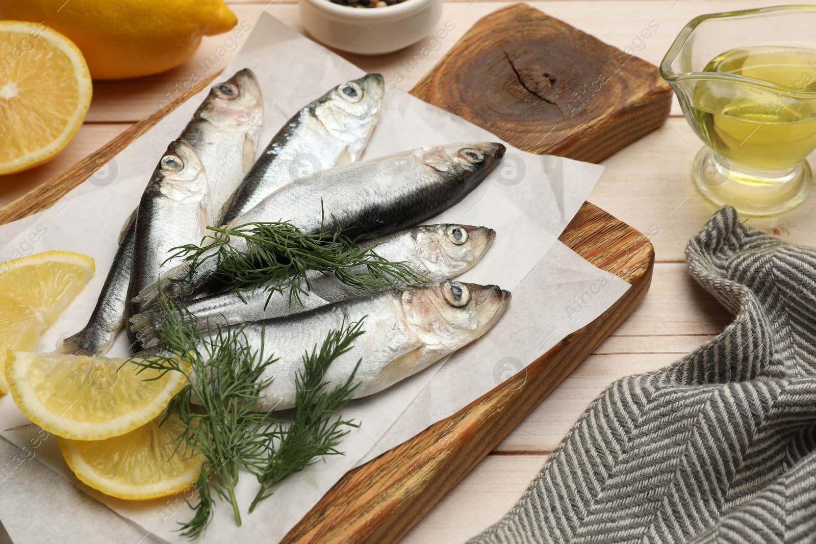 Photo of Fresh raw sprats, lemon and dill on light wooden table, closeup