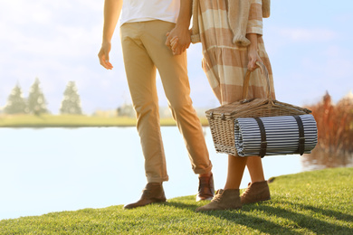 Young couple with picnic basket near lake on sunny day, closeup