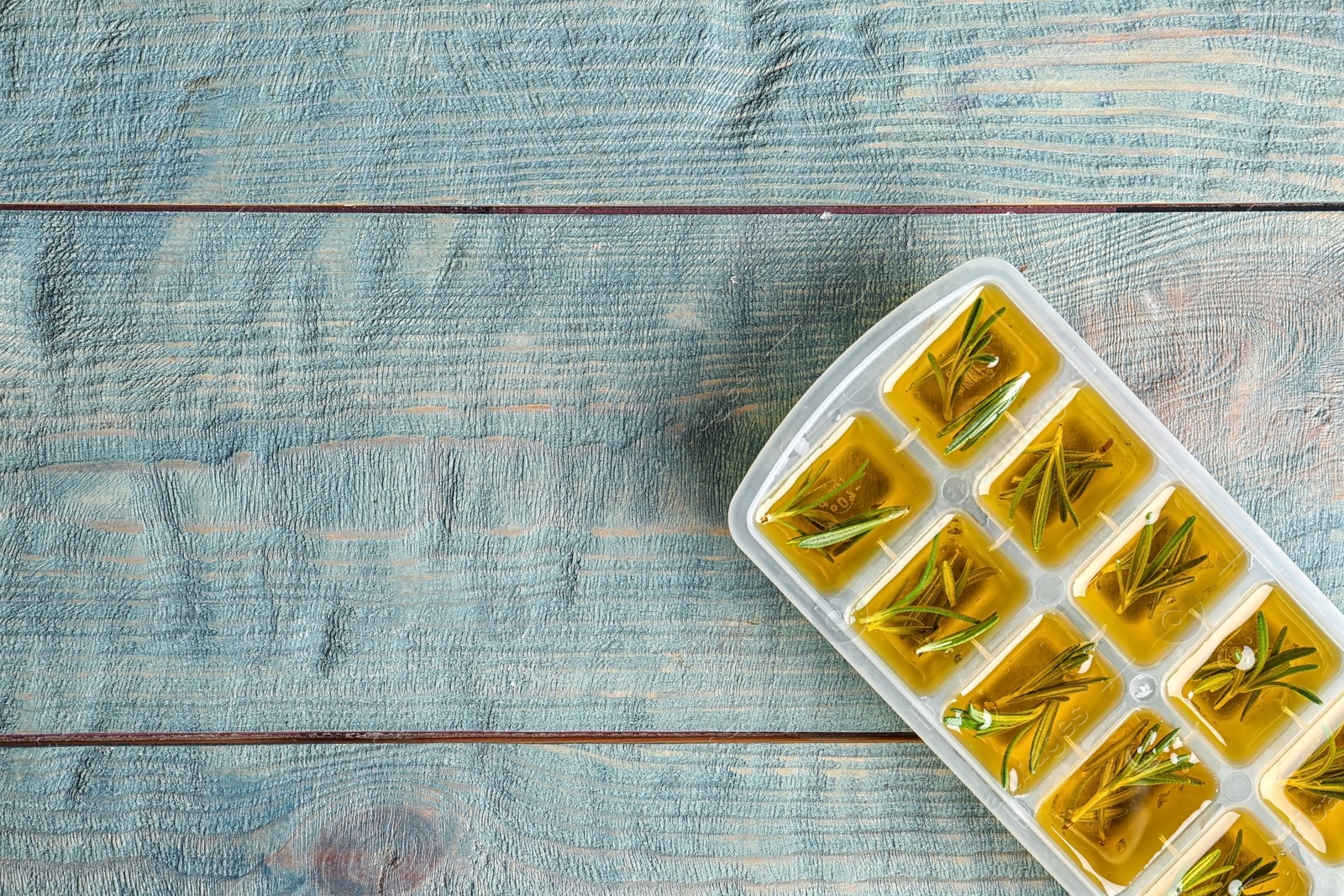 Photo of Ice cube tray with rosemary and olive oil on wooden background, top view. Space for text