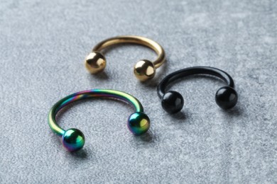 Photo of Stylish horseshoe rings on light grey table, closeup. Piercing jewelry