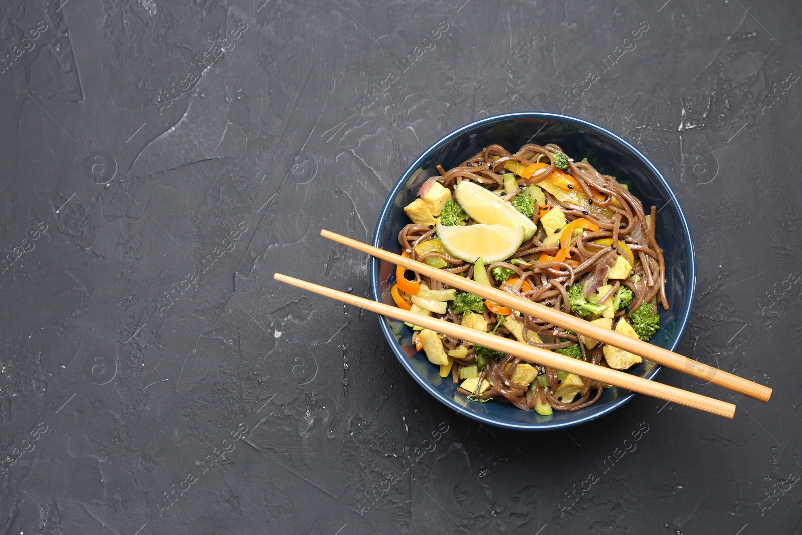 Photo of Stir-fry. Delicious cooked noodles with chicken and vegetables in bowl served on gray textured table, top view. Space for text