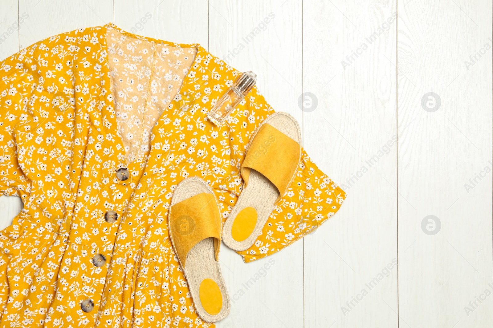 Photo of Stylish yellow dress, perfume and shoes on wooden floor, flat lay