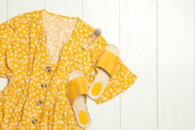 Stylish yellow dress, perfume and shoes on wooden floor, flat lay