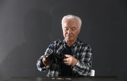 Photo of Poor elderly man with empty wallet and coins at table on dark background