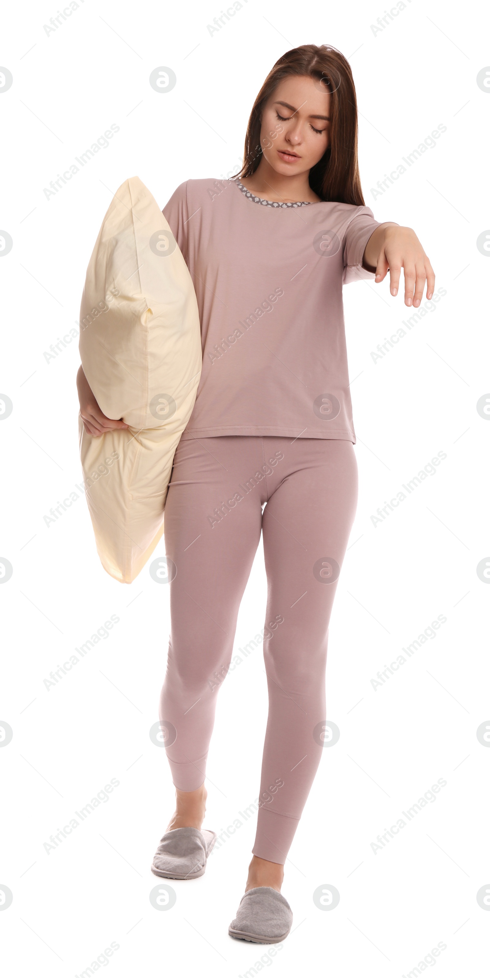 Photo of Young woman wearing pajamas and slippers with pillow in sleepwalking state on white background