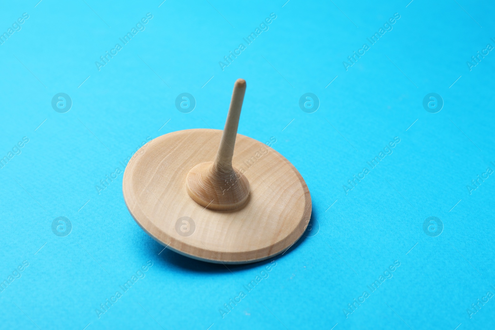 Photo of One wooden spinning top on light blue background, closeup. Space for text