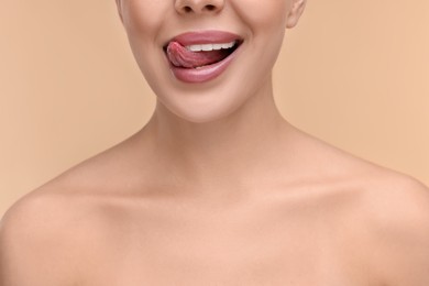 Photo of Woman with beautiful lips licking her teeth on beige background, closeup