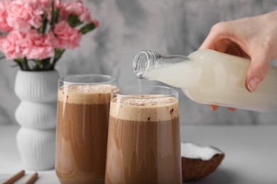 Woman pouring delicious coconut syrup into glass with coffee at table, closeup