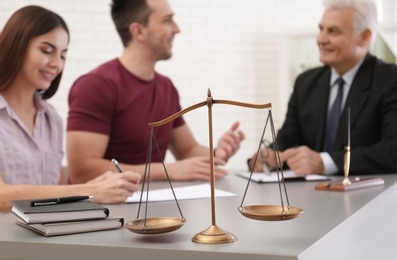 Photo of Lawyer having meeting with young couple in office, focus on scales of justice