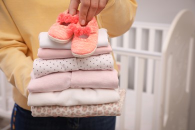 Woman holding stack of girl's clothes and booties indoors, closeup