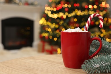 Photo of Christmas cocoa with marshmallows and candy cane in red cup on wooden table indoors, closeup. Space for text