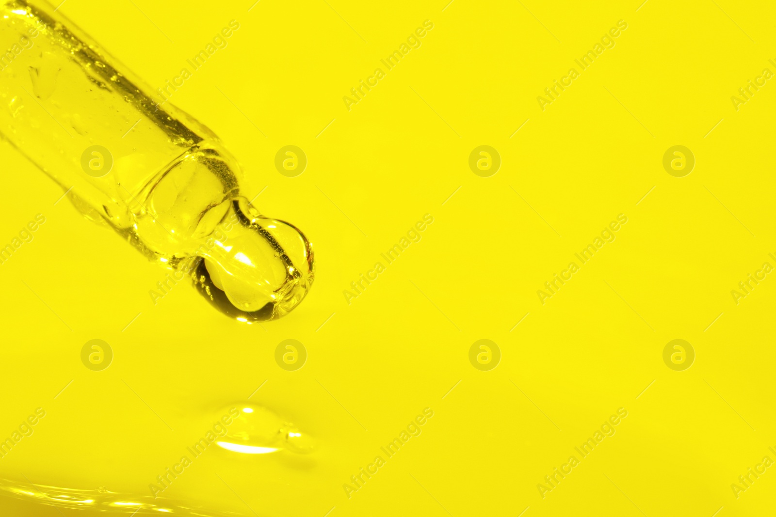 Photo of Dripping face serum from pipette on yellow background, closeup. Space for text