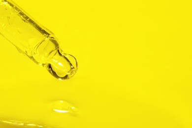 Photo of Dripping face serum from pipette on yellow background, closeup. Space for text