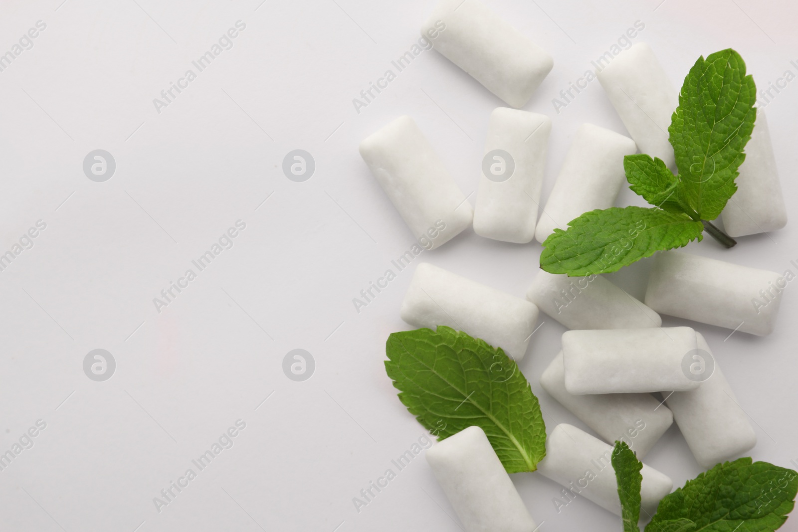 Photo of Tasty chewing gums and mint leaves on white background, top view. Space for text