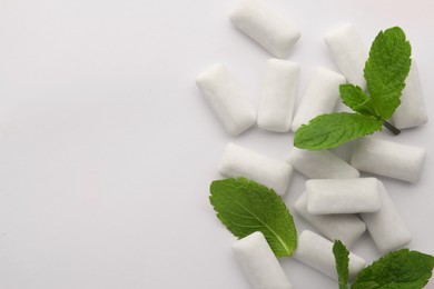 Tasty chewing gums and mint leaves on white background, top view. Space for text