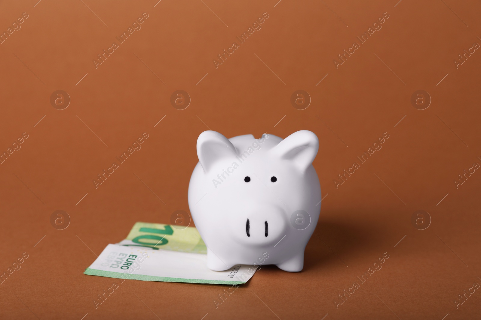 Photo of Ceramic piggy bank and euro banknote on brown background. Financial savings