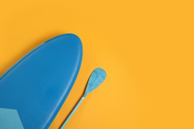 Photo of SUP board and paddle on yellow background, flat lay with space for text. Water sport