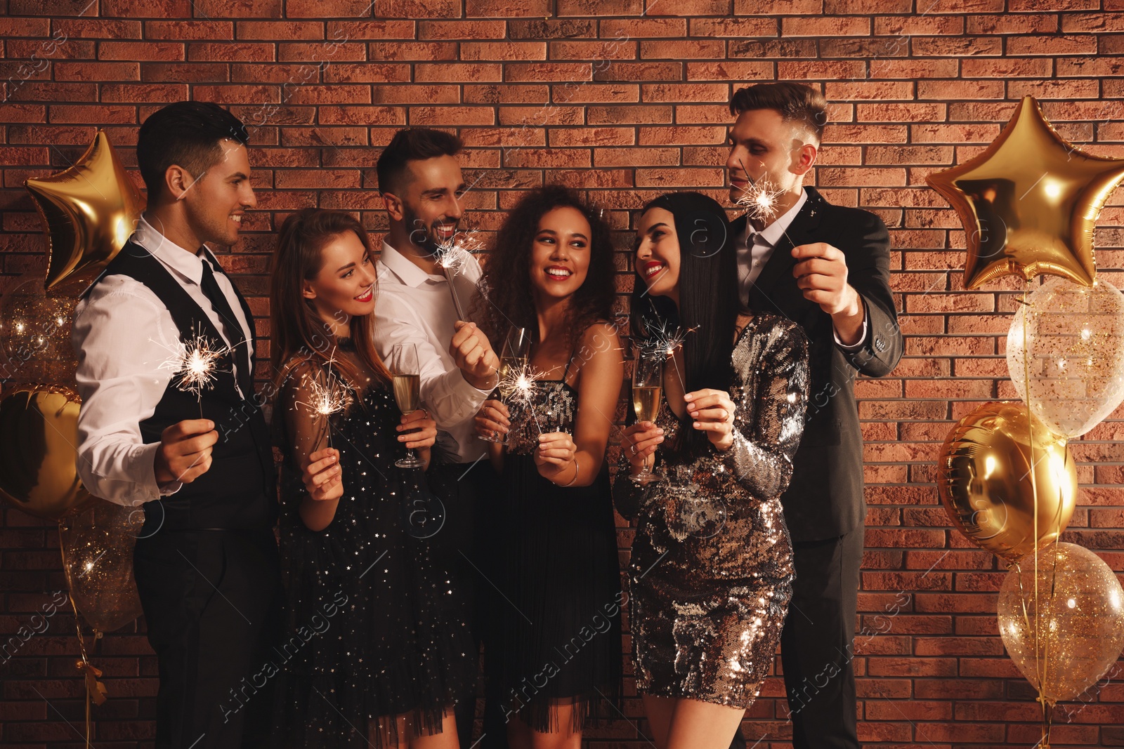 Photo of Happy friends with glasses of sparkling wine and sparklers celebrating New Year indoors