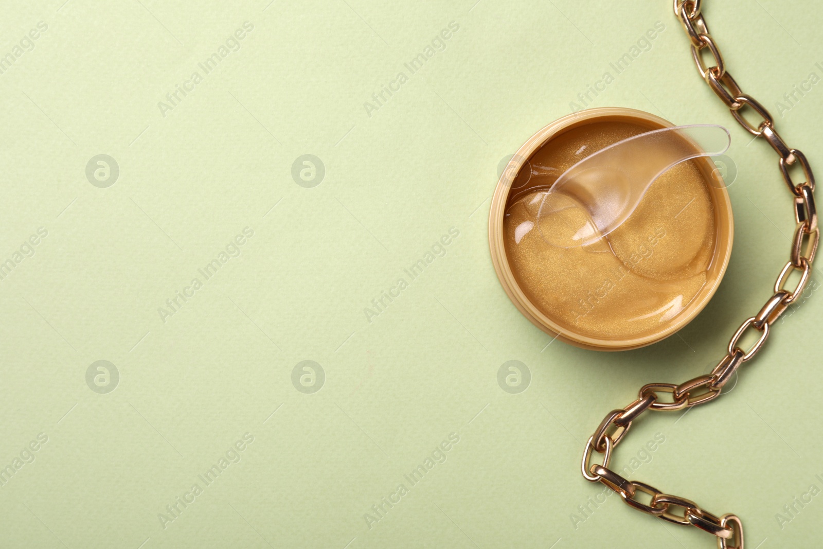 Photo of Under eye patches in jar with spatula and necklace on olive background, flat lay. Space for text