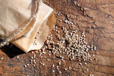 Photo of Paper bag with scattered tomato seeds on wooden background, top view. Vegetable planting