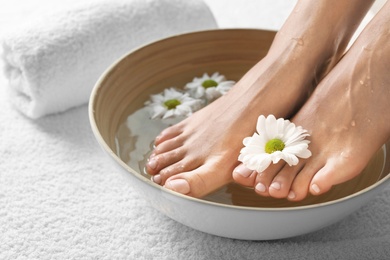 Photo of Closeup view of woman soaking her feet in dish with water and flowers on white towel. Spa treatment