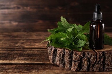 Glass bottle of nettle oil with dropper and leaves on wooden table. Space for text