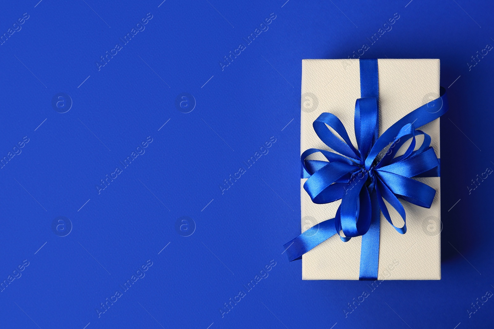 Photo of Beautiful gift box with bow on blue background, top view. Space for text