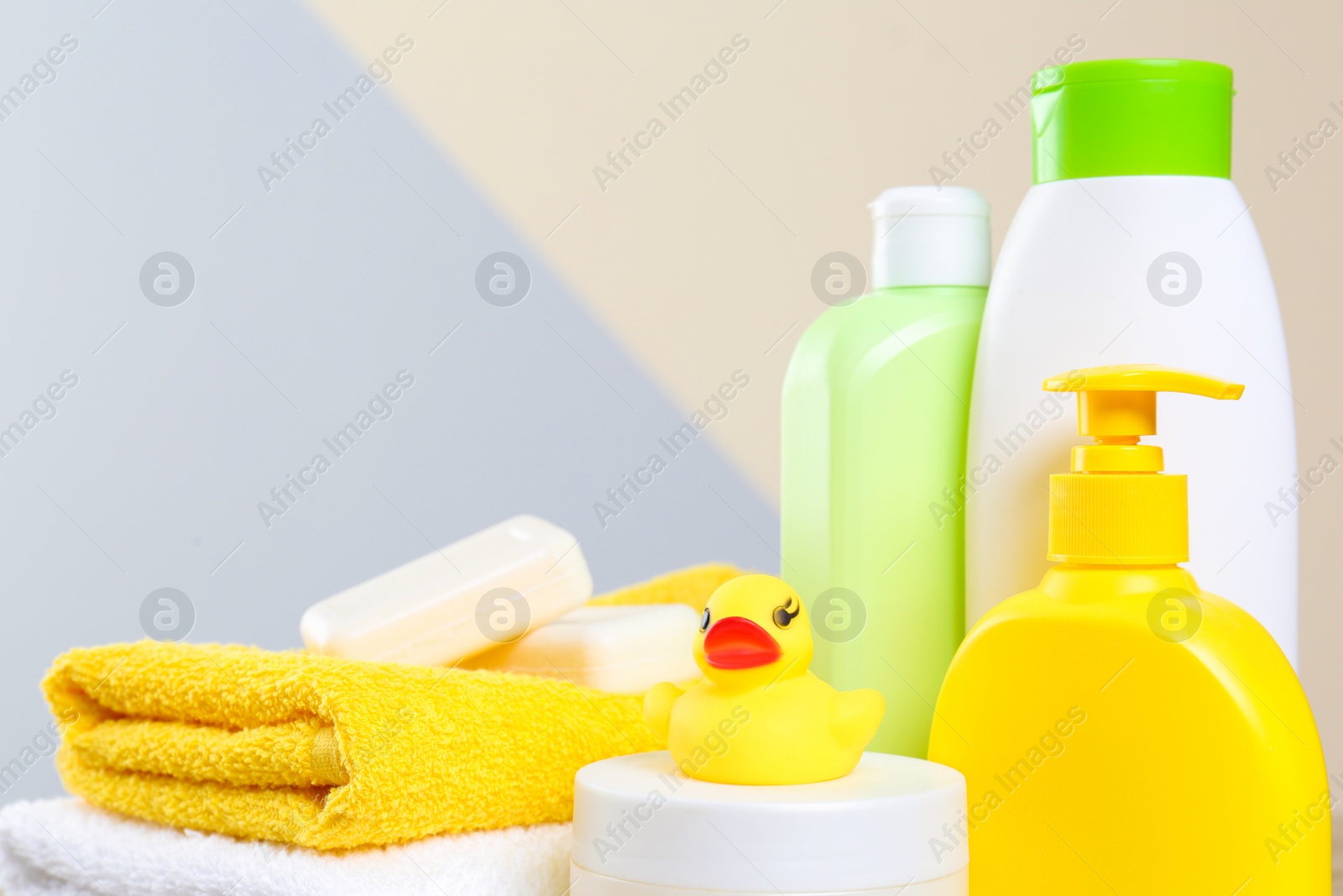 Photo of Baby cosmetic products, toy and towels against color background, closeup