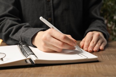 Woman writing in notebook at wooden table, closeup