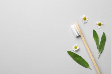 Photo of Bamboo toothbrush, beautiful chamomile flowers and fresh sage leaves on white background, flat lay. Space for text