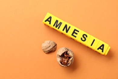 Photo of Word Amnesia made of yellow cubes and broken walnut on orange background, flat lay. Space for text
