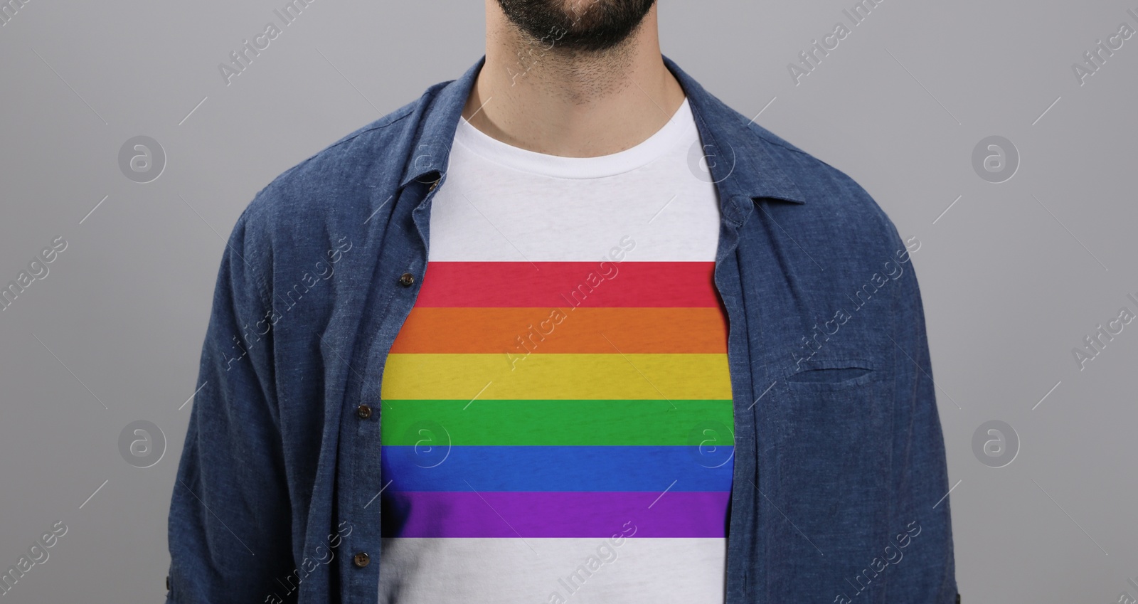 Image of Young man wearing white t-shirt with image of LGBT pride flag on light grey background, closeup
