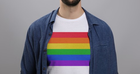 Young man wearing white t-shirt with image of LGBT pride flag on light grey background, closeup