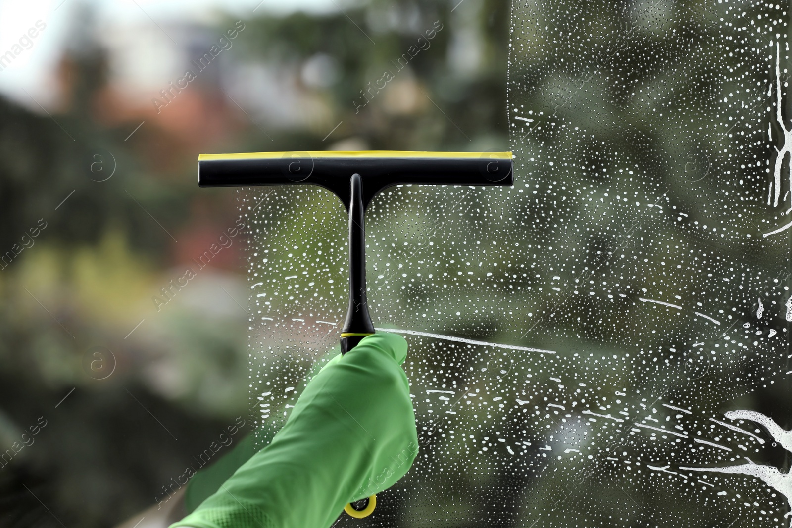 Photo of Woman cleaning glass with squeegee indoors, closeup