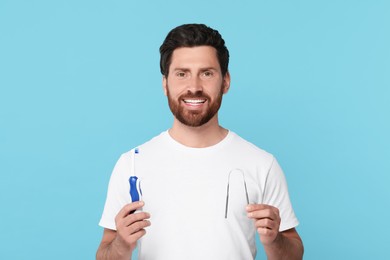 Happy man with tongue cleaner and electric toothbrush on light blue background