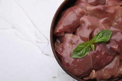 Photo of Bowl with raw chicken liver and basil on white textured table, top view. Space for text