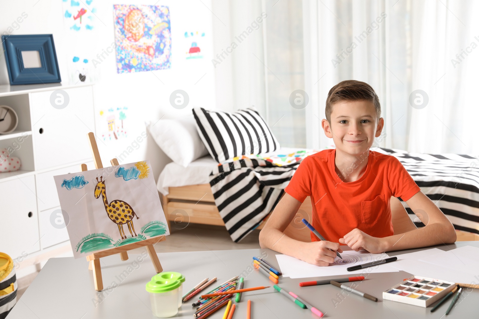 Photo of Little child drawing picture at table with painting tools indoors