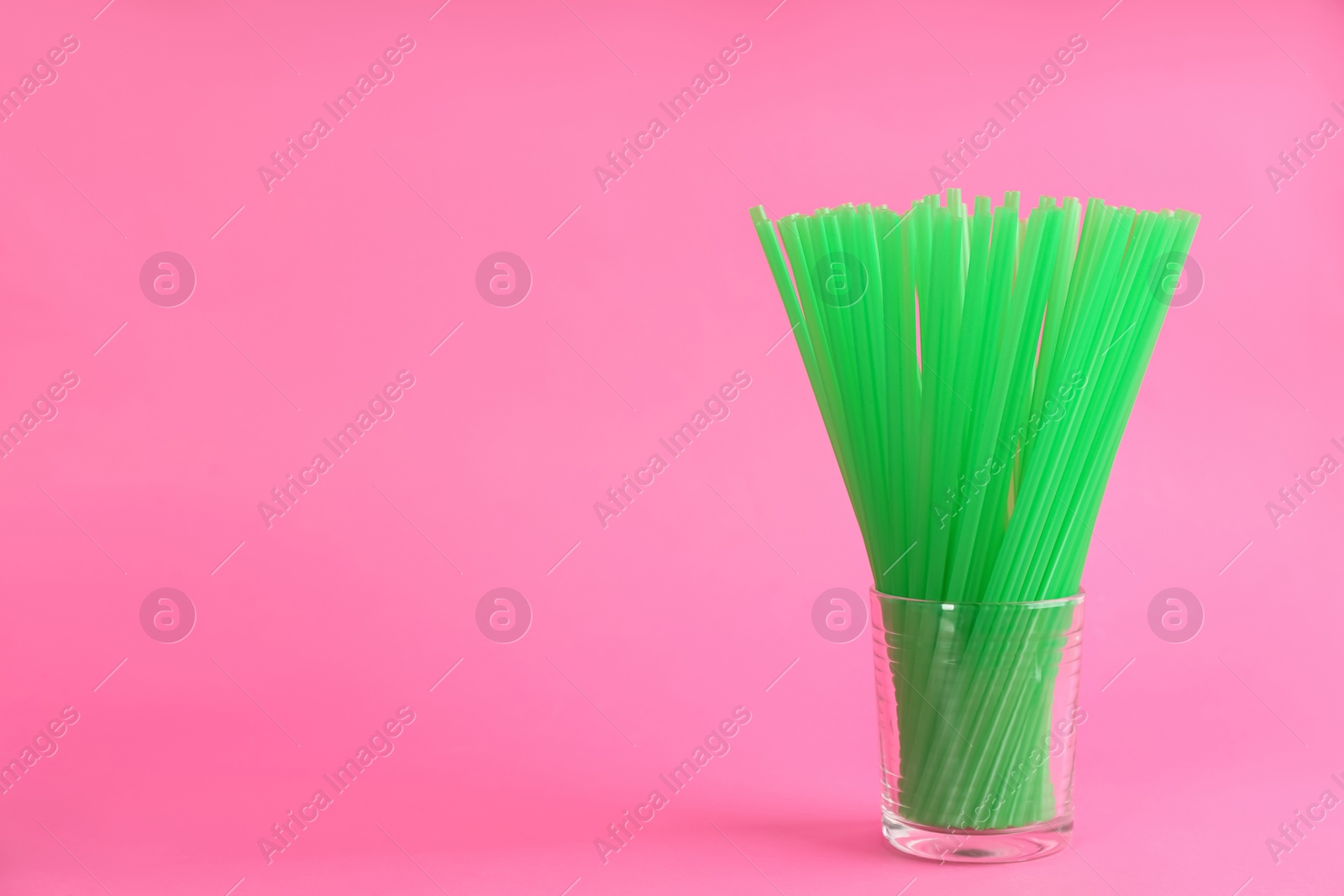 Photo of Green plastic drinking straws in glass on pink background, space for text