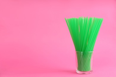 Photo of Green plastic drinking straws in glass on pink background, space for text