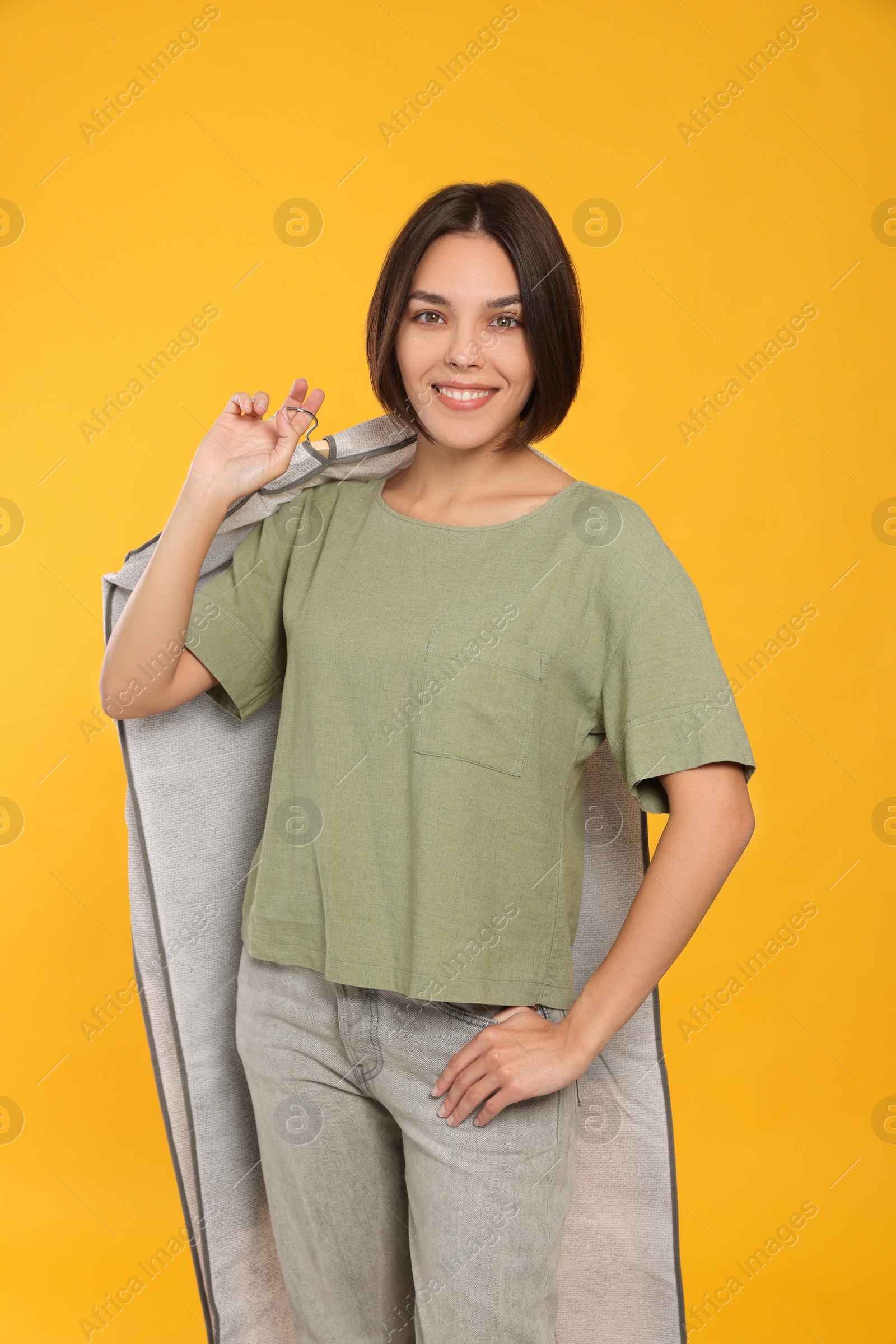 Photo of Woman holding garment cover with clothes on yellow background. Dry-cleaning service