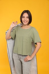 Woman holding garment cover with clothes on yellow background. Dry-cleaning service